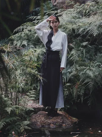 一位穿着白色衣服的女子站在一条溪流中的岩石上