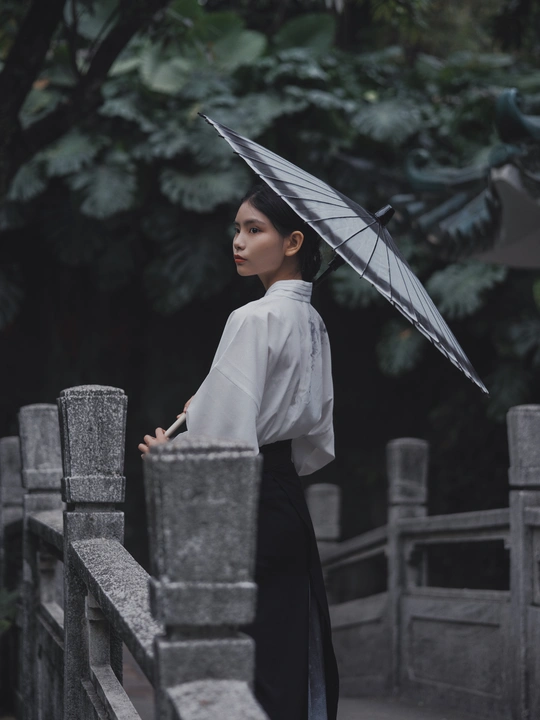 一位女士站在桥上 手里拿着一把黑色雨伞。