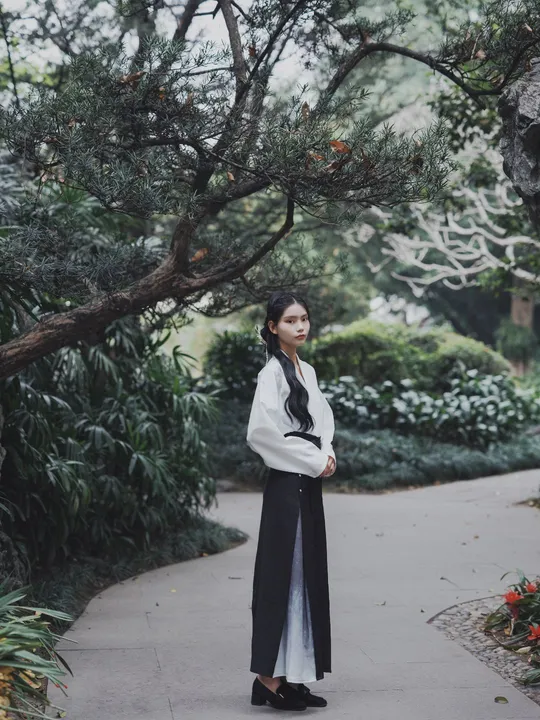 一位穿着全白衣服的女人站在一个花园里的长人行道上。