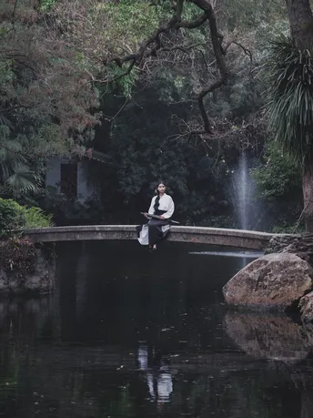 一个男子和一个女子坐在池塘上的桥上 背景有瀑布。