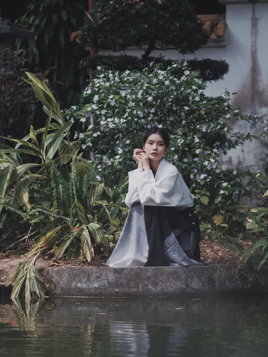 一个穿着长袍的女人坐在河边一块岩石上