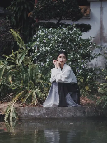 一个穿着长袍的女人坐在河边一块岩石上