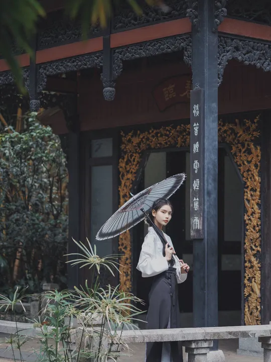 一位女士拿着黑色雨伞站在一栋建筑前