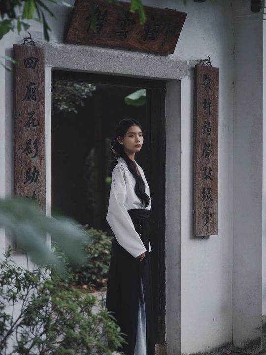 一位穿着白色长袍的年轻女子站在一座传统建筑的门口