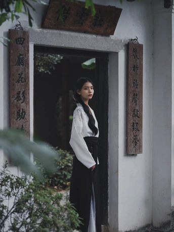 一位穿着白色长袍的年轻女子站在一座传统建筑的门口