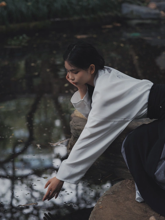 一个年轻女孩坐在河边的岩石上 凝视着水面。