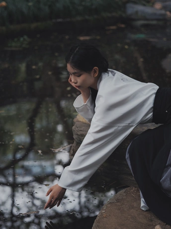 一个年轻女孩坐在河边的岩石上 凝视着水面。