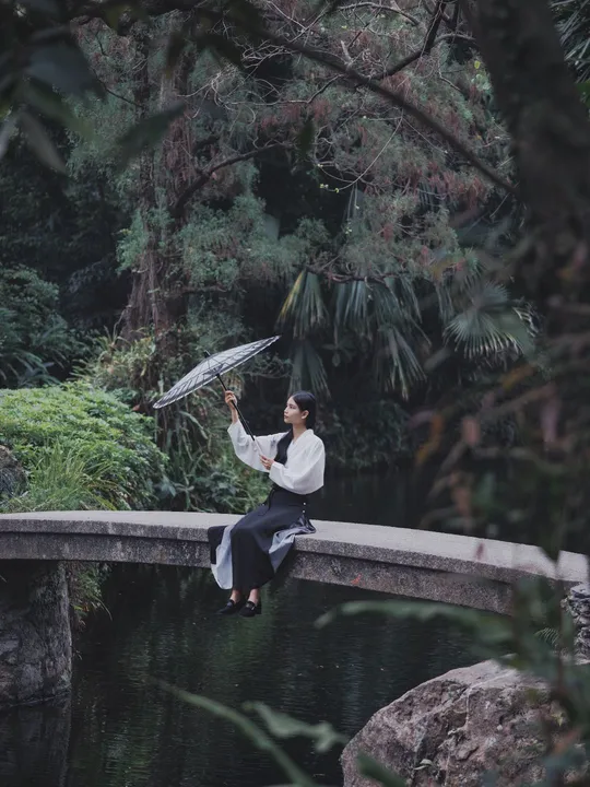 一位女士在河上的桥上拿着一把伞