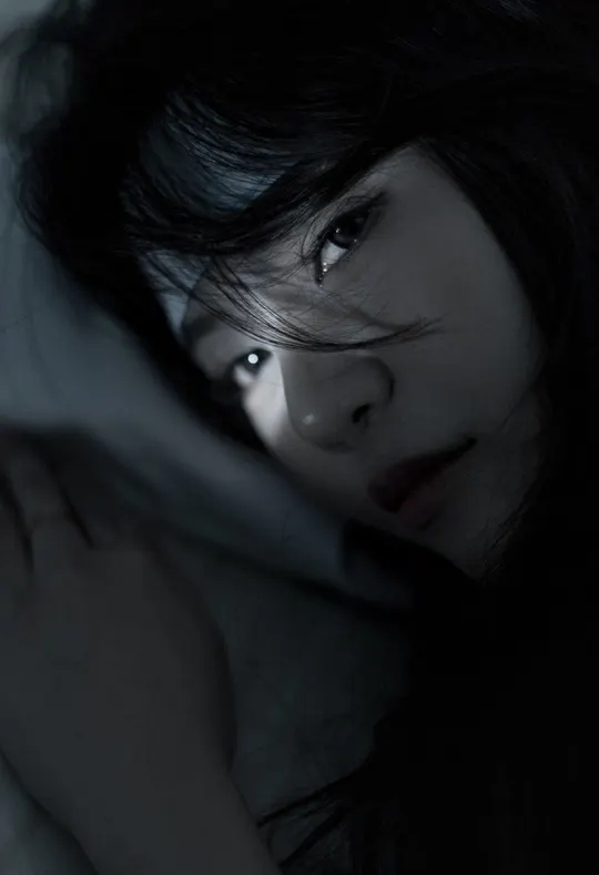 一个年轻女子躺在黑暗的床上 双手捂住脸
