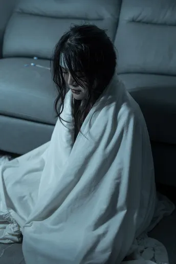 一个穿着白色长袍的女人坐在地板上 脸上盖着毛毯。