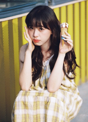 一个穿着黄白色裙子的年轻女子拿着冰淇淋 cone。