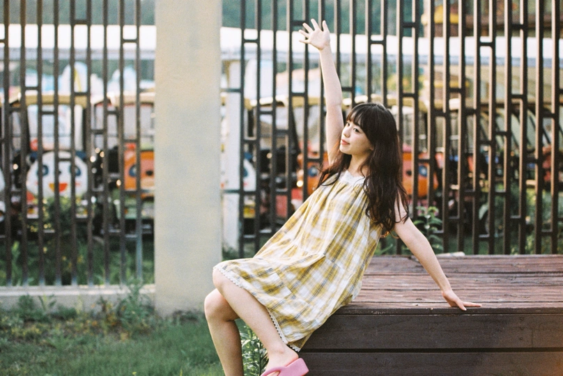 一位穿着黄色连衣裙的年轻女子坐在公园里的木凳上
