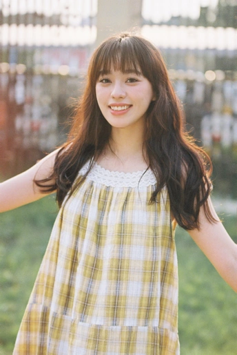 一位穿着黄色格子衬衫的年轻女子站在外面 伸开双臂。