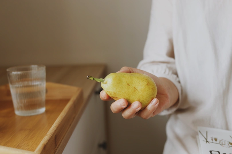 左手拿着一个青苹果或梨 面前桌子上放着一杯水的女人