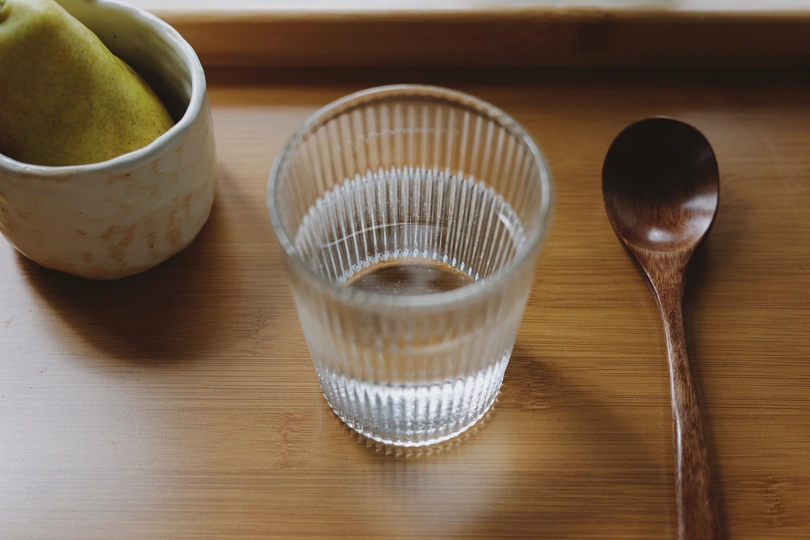 一张木桌 里面有一碗水果、一个塑料杯、一把勺子和一杯水