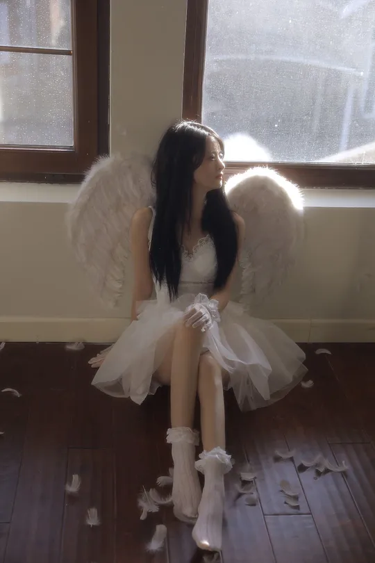 一个穿着白色连衣裙带有翅膀的年轻女子坐在窗户前地板上