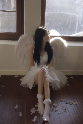 一个穿着白色连衣裙带有翅膀的年轻女子坐在窗户前地板上