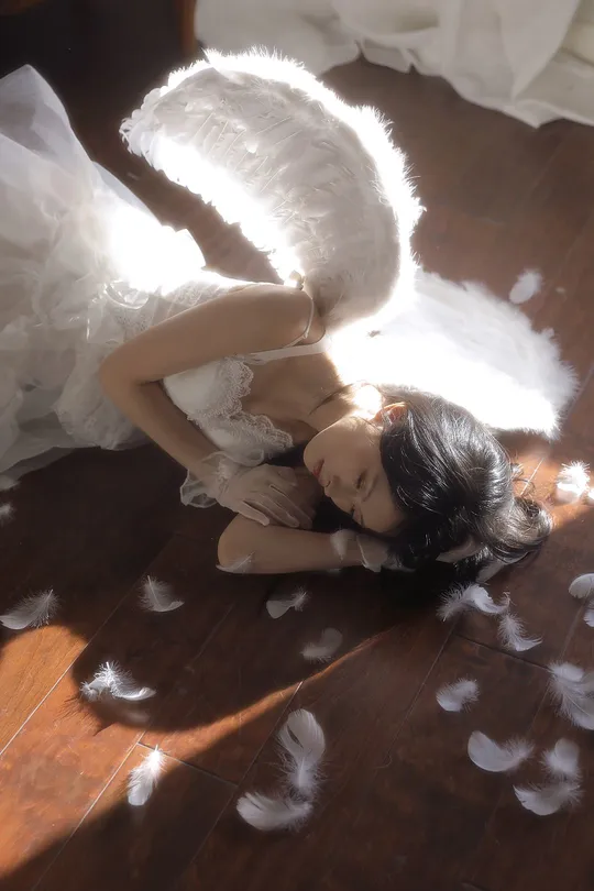 一个穿着白色裙子的年轻女子躺在地上 翅膀上有羽毛 一个小天使也躺在地上。
