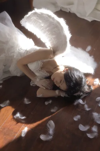 一个穿着白色裙子的年轻女子躺在地上 翅膀上有羽毛 一个小天使也躺在地上。