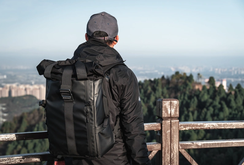 一个人背着书包坐在山顶的长椅上 眺望着城市。