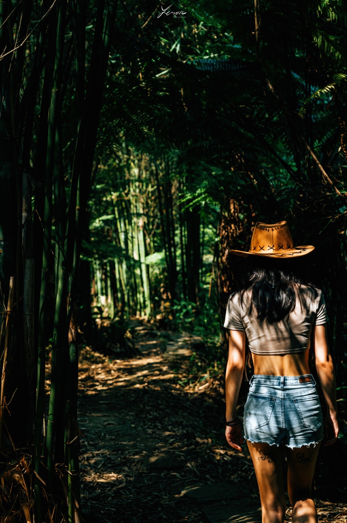 一位戴牛仔帽的女人穿过森林小径走向森林。