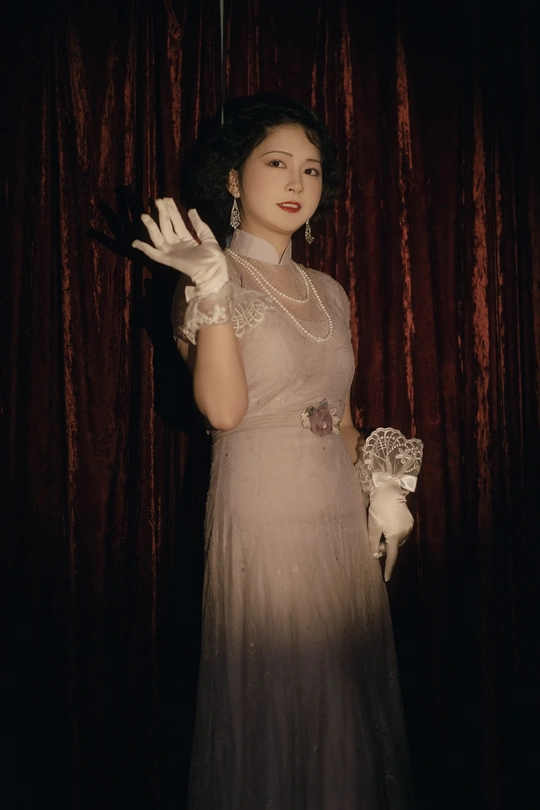 一位穿着长袍和手套的女人站在窗帘前