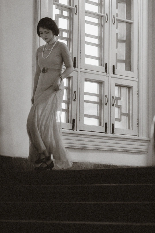 一位穿着白色连衣裙的女人站在一些台阶前 门和窗户的后面。
