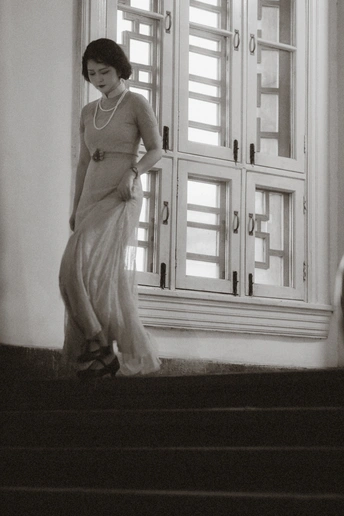 一位穿着白色连衣裙的女人站在一些台阶前 门和窗户的后面。