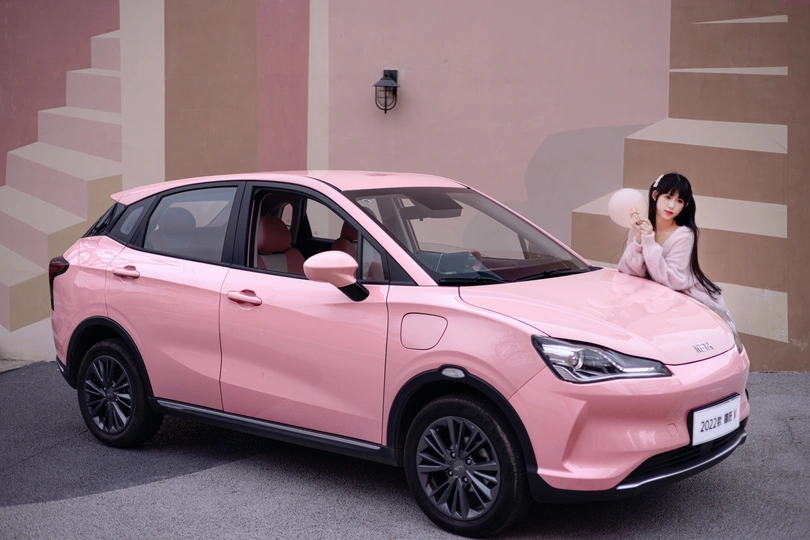 一位女性坐在粉红色的Smart Car内 背景有一位女模特。