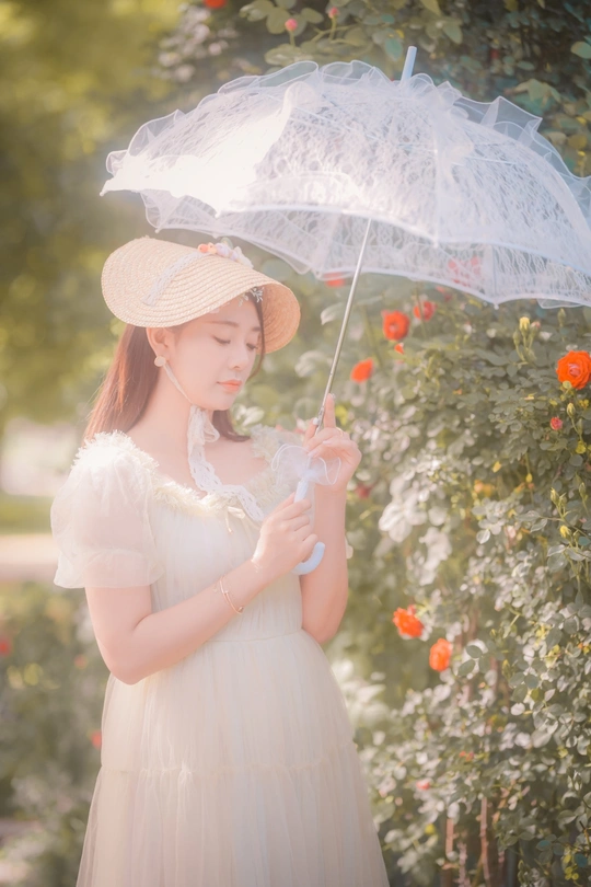 一个小女孩穿着白色连衣裙和帽子 拿着透明的雨伞