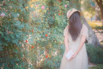 一位穿着白色连衣裙的年轻女子站在花园里 手里拿着一本书。
