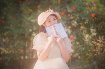一个小女孩穿着白色裙子 手里拿着一本书 在花园里。