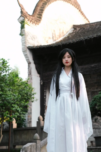 一个穿着白色长裙的年轻女子站在一栋楼前