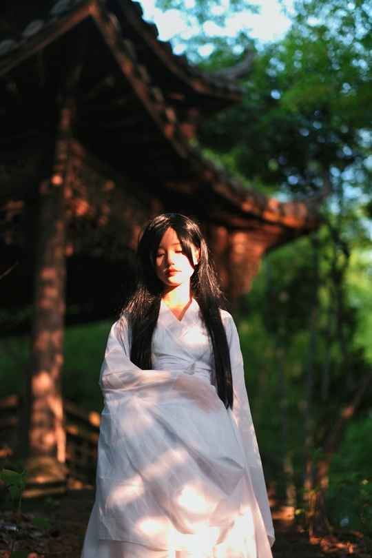 一个穿着白色连衣裙的年轻女子站在树林里