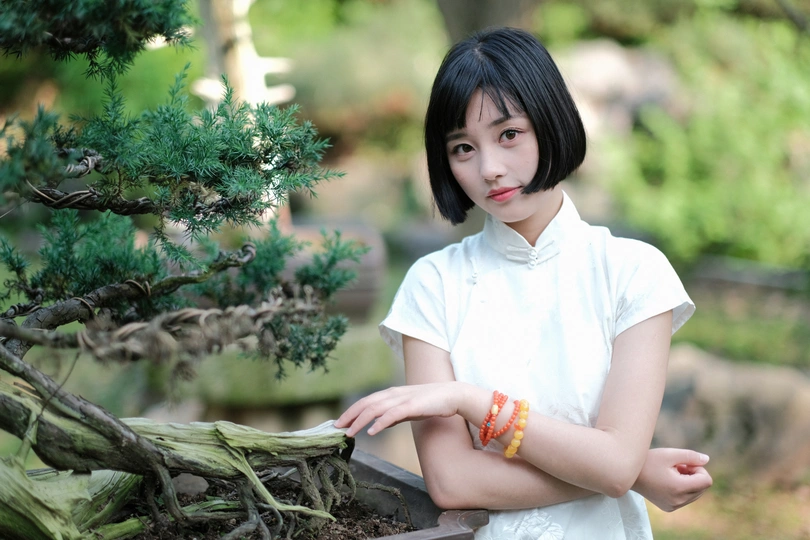 花园里一个穿着白色连衣裙的年轻女子手里拿着一株小植物