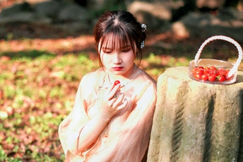 一个穿着白色衣服的年轻女孩站在树桩旁 手里拿着一篮草莓和苹果