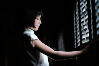 一个年轻女人在黑暗的房间里看着窗外 把手伸到手臂上