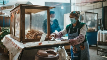戴着手套和面罩的女人站在一张桌子前 桌子上有一些食物。