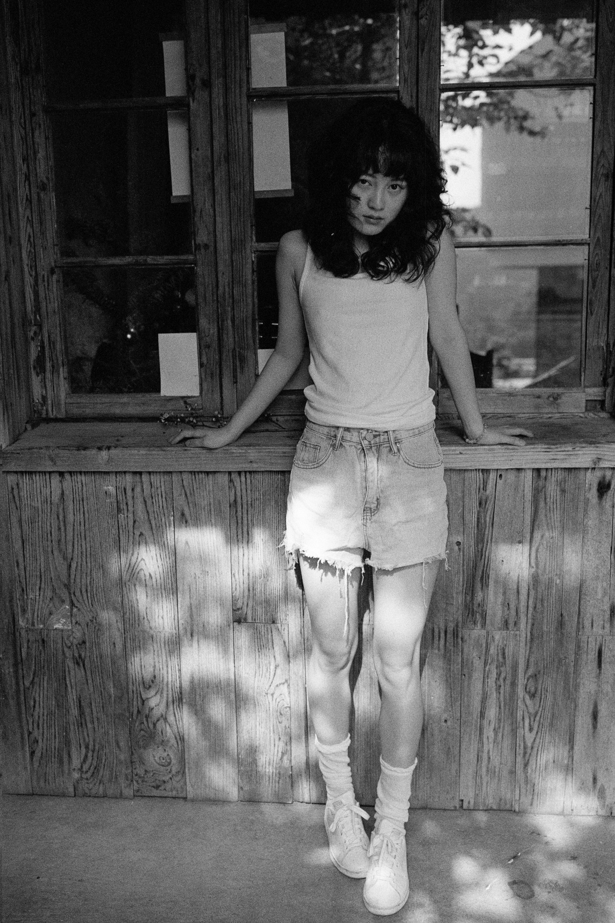一张黑白照片 照片中一个年轻女孩站在一所房子的门廊上 双腿靠在窗户上