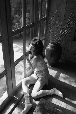 一个年轻女孩坐在门廊上看着窗外的花瓶