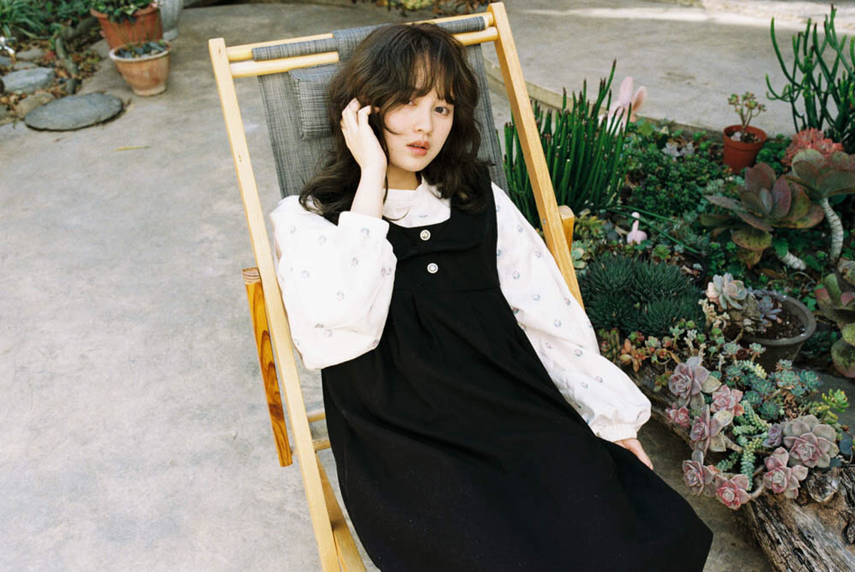 一个穿着黑色连衣裙的年轻女子坐在一个有盆栽的花园长椅上