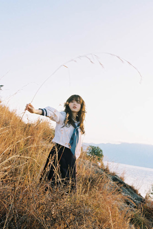 一个穿着领带的女孩站在山丘上 双臂伸展在一片草地上 靠近海洋。