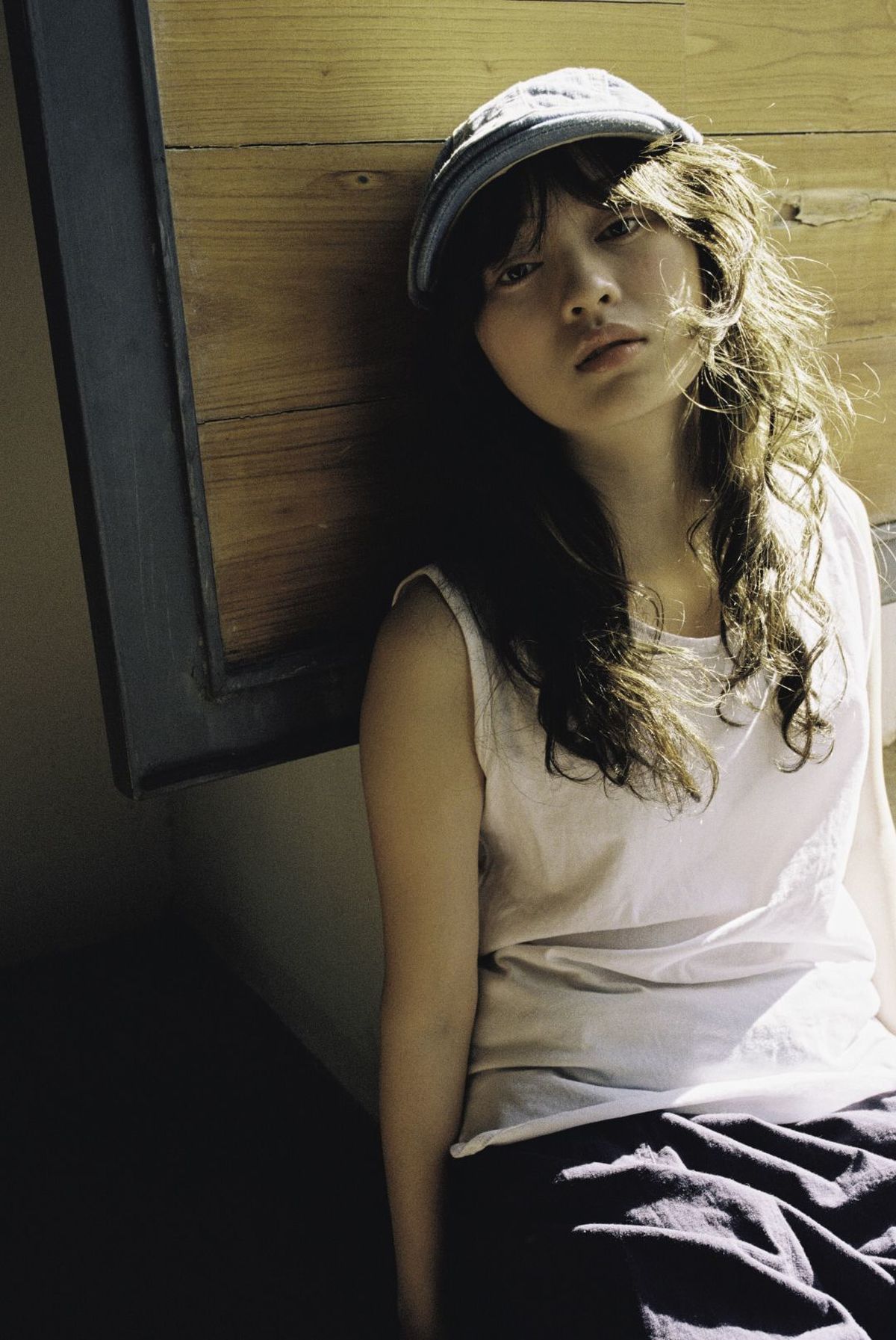 一个年轻女子穿着一顶白色棒球帽 坐在床边 靠在一面带有木制护墙板的墙壁上。