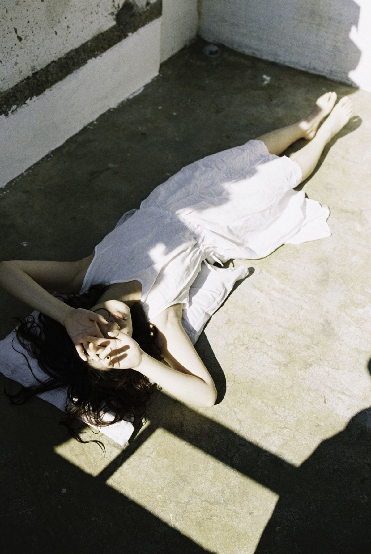 一个穿着白色连衣裙的年轻女子躺在建筑物地板上