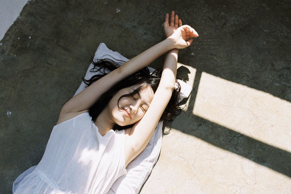 一个穿着白色连衣裙的年轻女子躺在地上 双手举过头顶