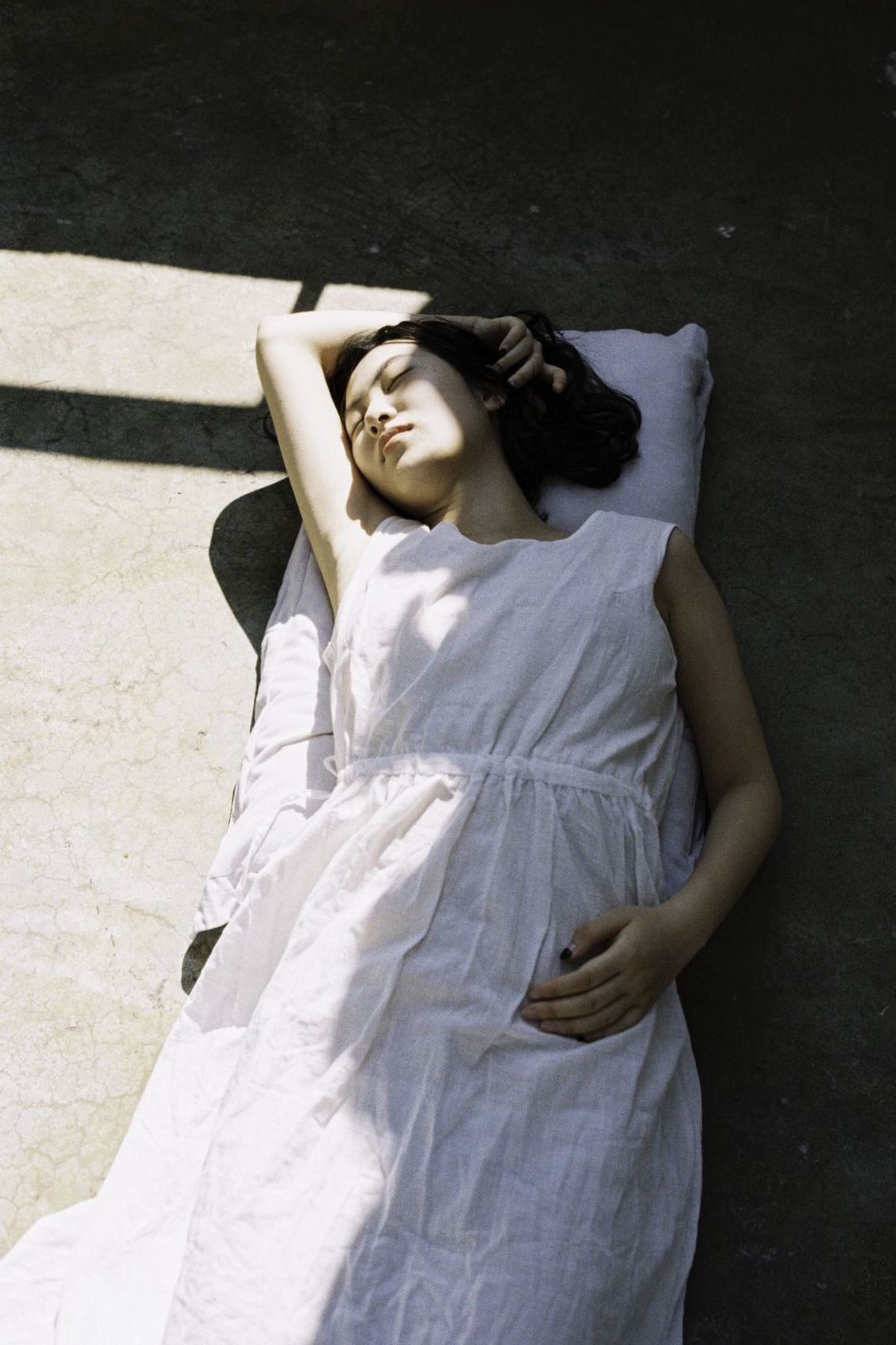 一个穿着白色连衣裙的年轻女子躺在地板上的阳光下