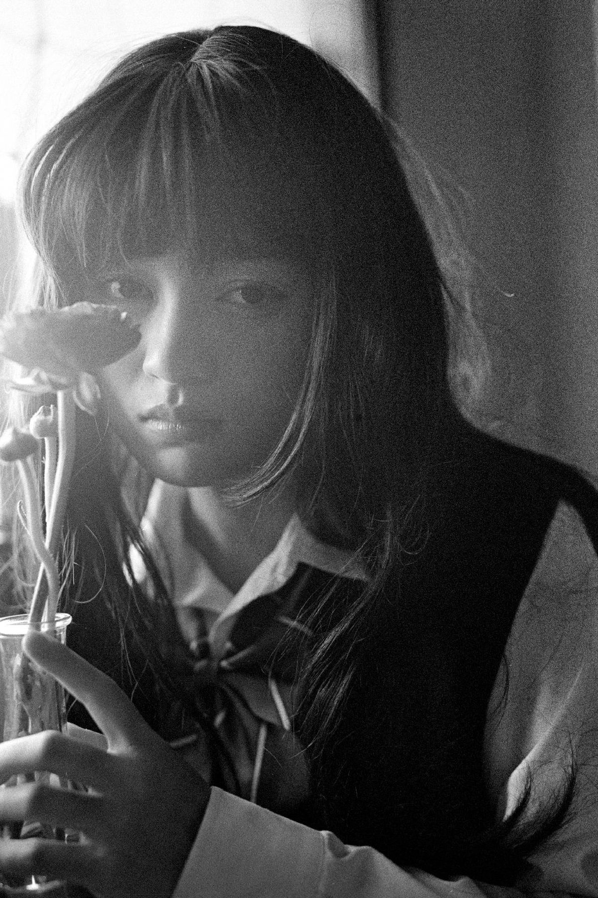 一个小女孩拿着一个装满水的玻璃杯和一束花在花瓶里。