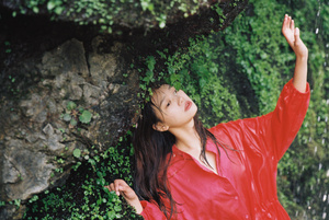 一位穿着红色连衣裙和雨伞的年轻女子在瀑布和岩石附近拍照