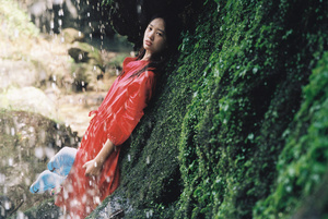 一位穿着红色连衣裙的年轻女子躺在瀑布旁一块岩石上