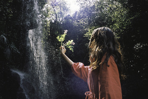 一个小女孩拿着花站在森林中的一处瀑布前